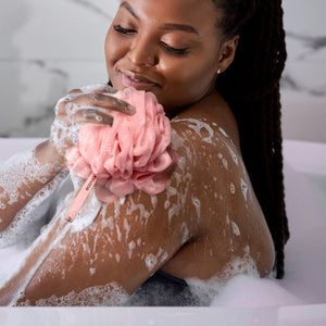 Pink ruffled bath sponge loofah held under water, creating lather