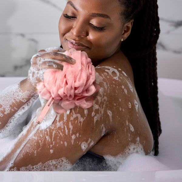 Pink ruffled bath sponge loofah held under water, creating lather
