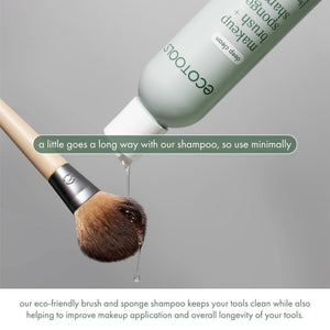 Sage-green shampoo bottle dispensing onto makeup brush bristles with foamy cleanser