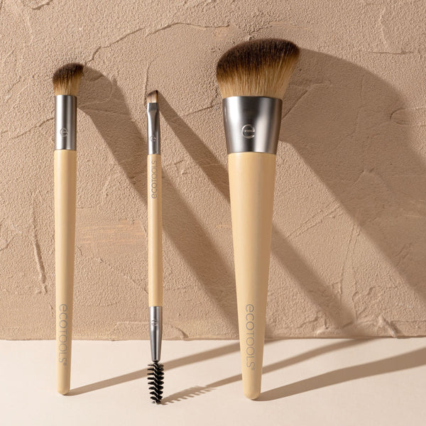 Three face makeup brushes with beige handles and silver ferrules on a textured surface