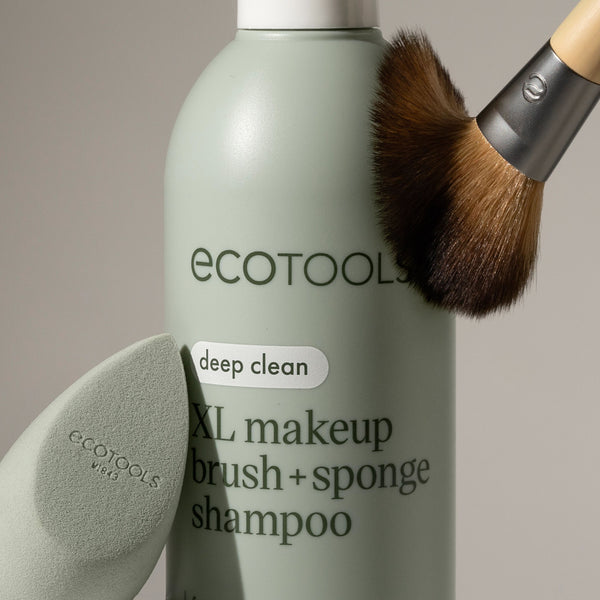 Sage-green shampoo bottle with deep clean label, makeup brush head and sponge nearby