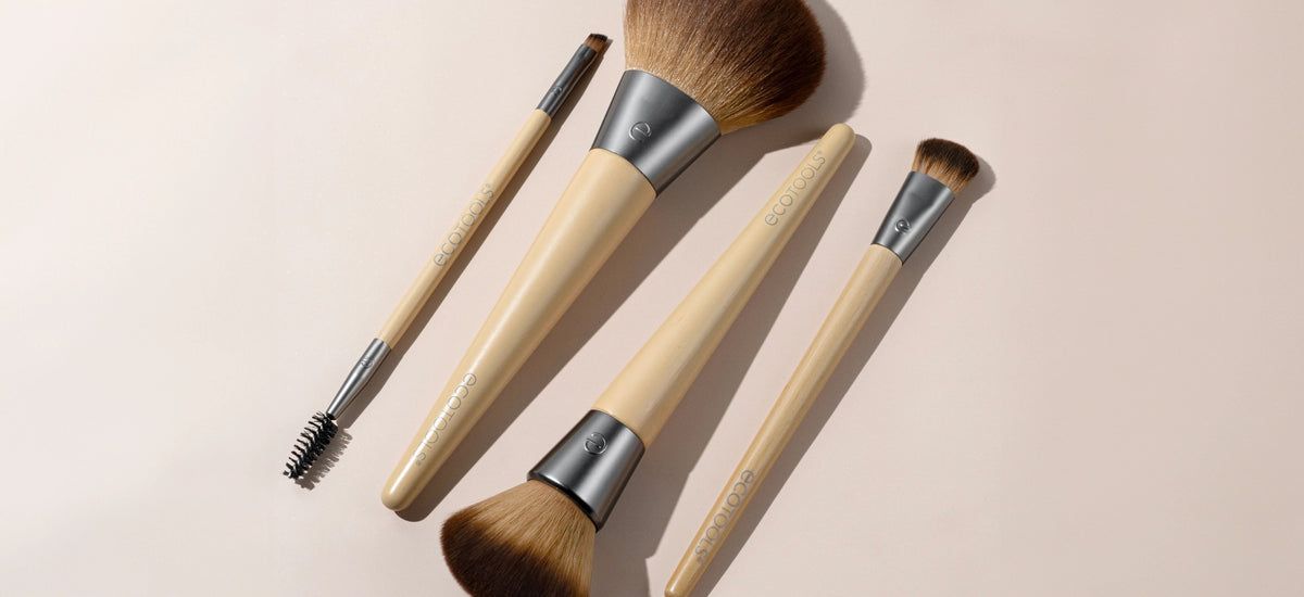 Makeup brushes with beige handles and brown bristles, arranged on a light pink background