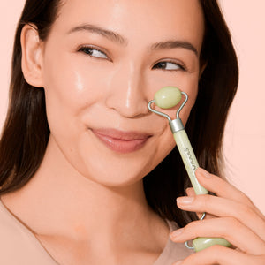 Facial roller with pale green jade stone and stainless frame, held near cheek