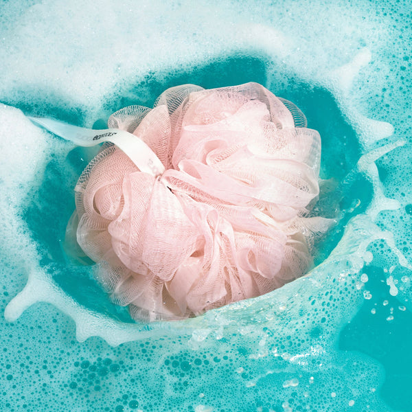 Delicate bath sponge made of soft pink fibers, soaking in water with bubbles
