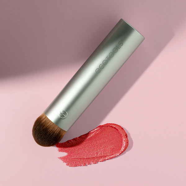 Makeup blending brush with domed brown bristles, light mint handle, and red cream swatch