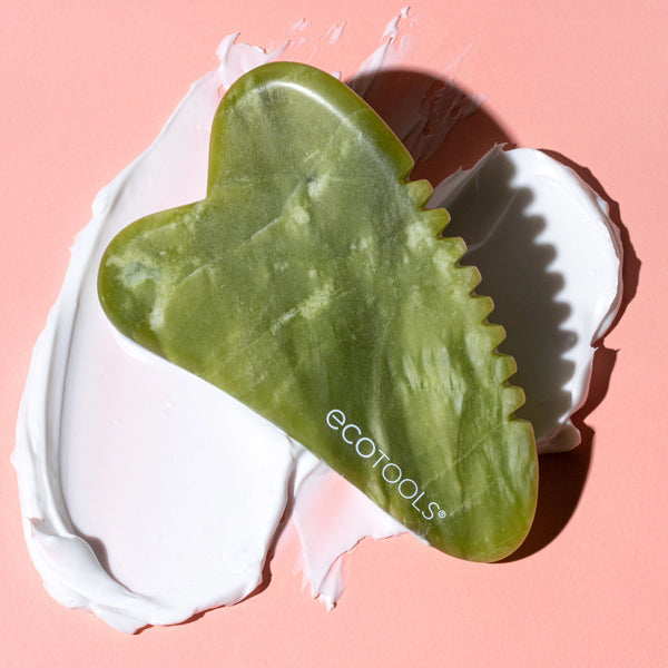 Jade gua sha stone resting on a white cloth with scalloped edge