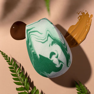 Green-and-white marbled teardrop facial blending sponge on a tabletop.