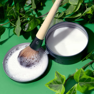 Green container with white cleaner and makeup brush making foam on soap dish