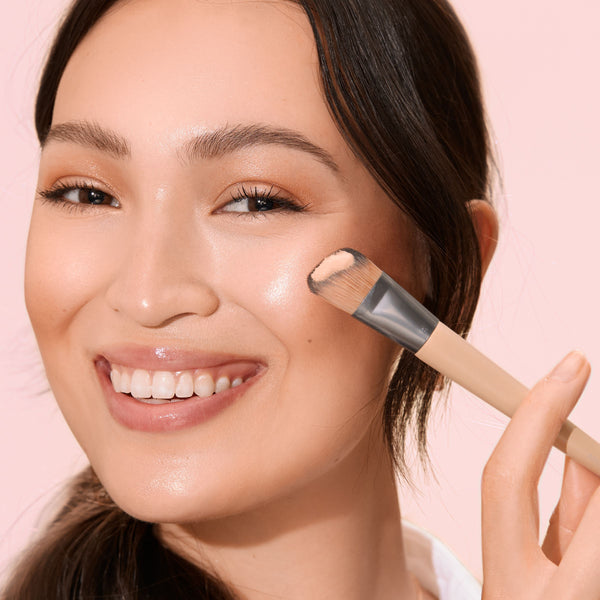 Makeup brush with beige handle and silver ferrule, soft brown bristles applying foundation
