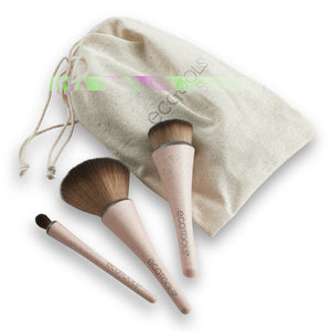 Three compact makeup brushes with beige handles and brown bristles beside beige pouch