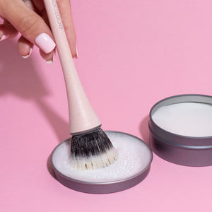 Foundation brush dipped in powder with soft bristle head on light pink handle