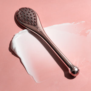 Rose-gold massage tool over cream, textured head visible