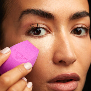 Purple makeup sponge held in fingers, dabbing near the eye area for blending